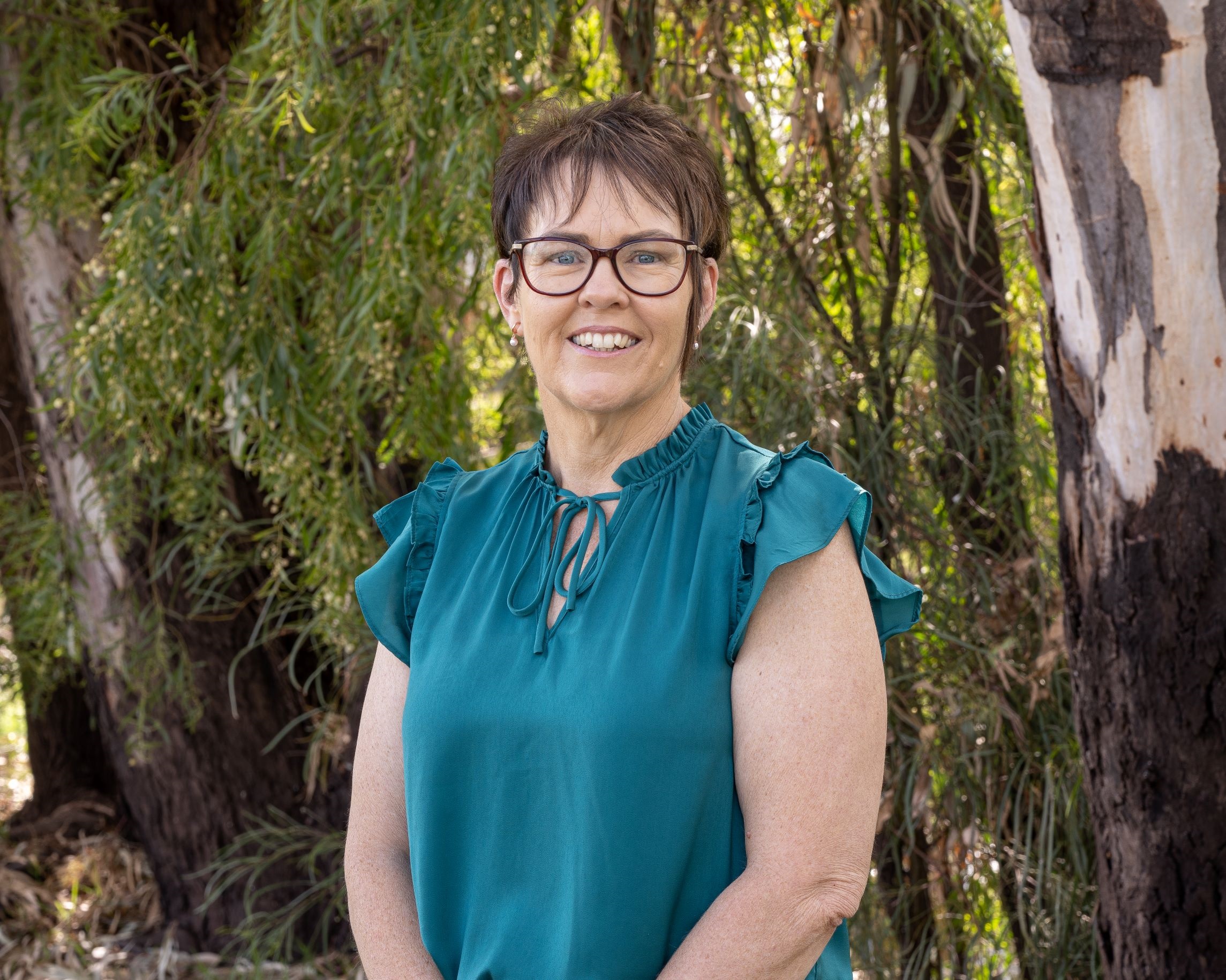 CEO Jodie Taylor wears a dark green shirt and smiles in front of Dalby trees and greenery.